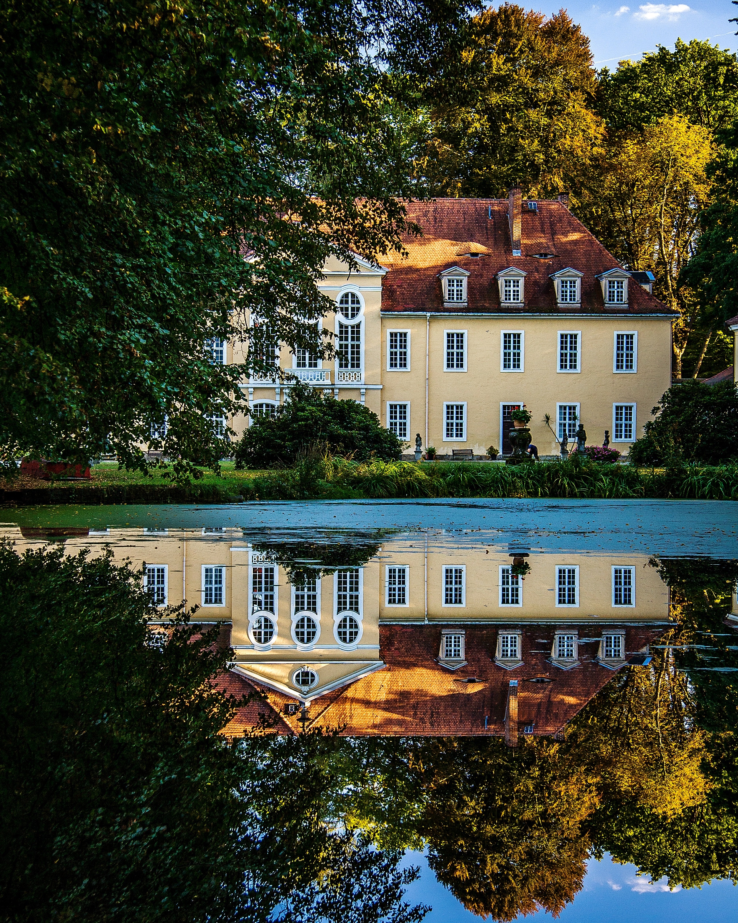 Historisch landhuis weerspiegeld in een vijver, omzoomd door bomen